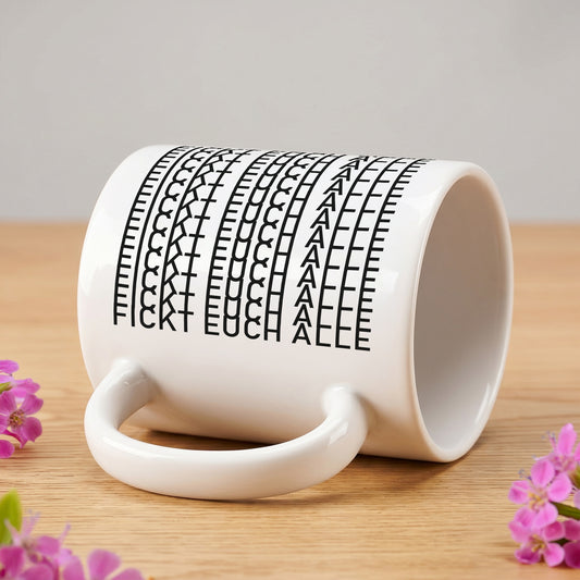 Seitlich liegende Tasse mit versteckter Botschaft „F*ckt euch alle“ auf Holztisch mit Blumen