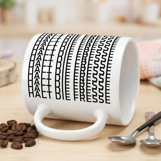 Liegende weiße Tasse mit sichtbarer versteckter Botschaft „Halt die Fresse“ im schwarzen Buchstabenmuster