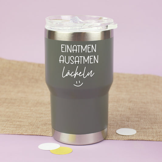 Grauer Thermobecher mit Deckel und Spruch Einatmen Ausatmen Lächeln auf hellem Hintergrund
