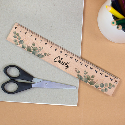 Personalisiertes Holzlineal mit Eukalyptusmotiv und Name Charly neben Schere und Stiftehalter