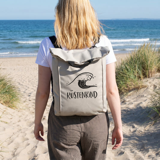 Beiger Rucksack mit Wellenmotiv und Wunschtext Küstenkind am Strand getragen