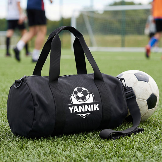 Schwarze Fußball Sporttasche mit Name Yannik auf dem Sportplatz