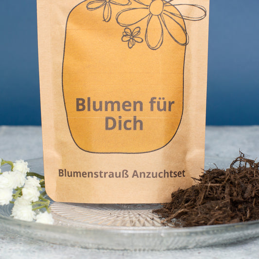 Detailaufnahme vom Blumen für Dich Anzuchtset mit Aufdruck Blumen für Dich und Blumenstrauß Anzuchtset, daneben Kokoserde und kleine weiße Blüten