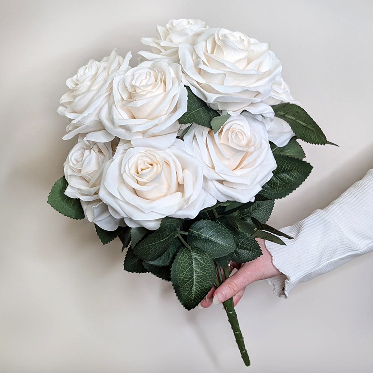 Hand präsentiert einen künstlichen Rosenstrauß mit weißen Blüten vor hellem Hintergrund