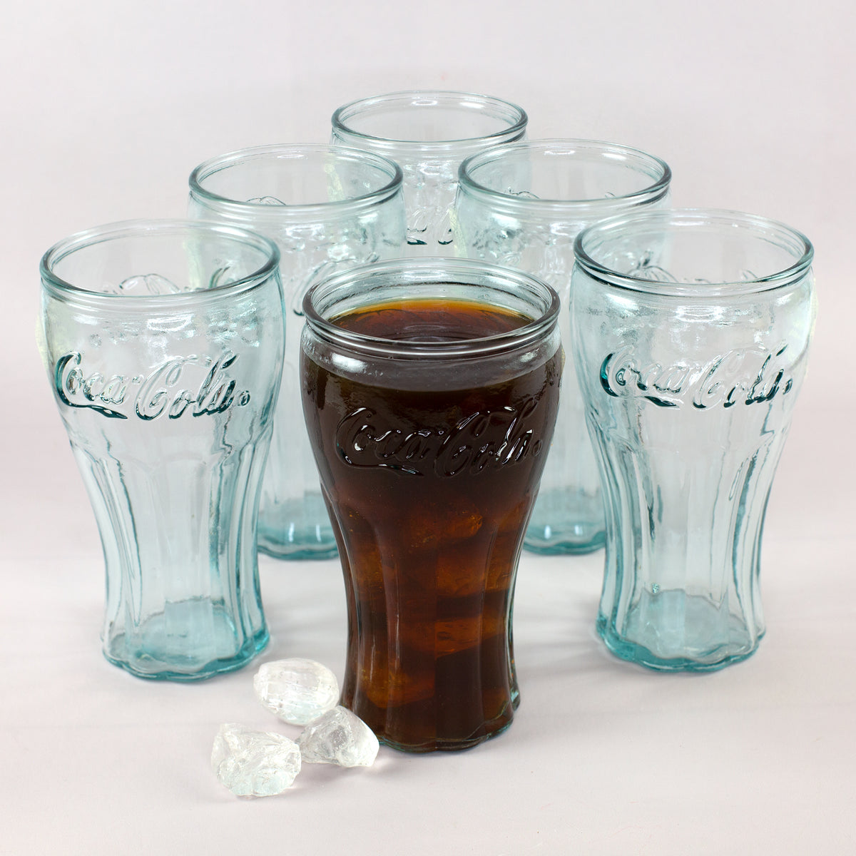 Coca-Cola Gläser Set mit fünf leeren Gläsern und einem gefüllten Glas mit Cola und Eiswürfeln