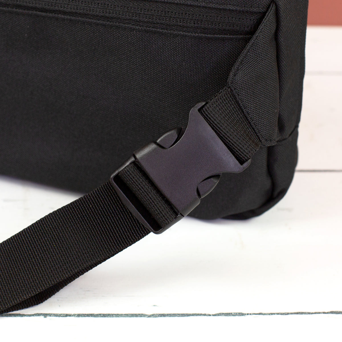 Detailansicht vom schwarzen Clipverschluss und verstellbarem Gurt der Bauchtasche