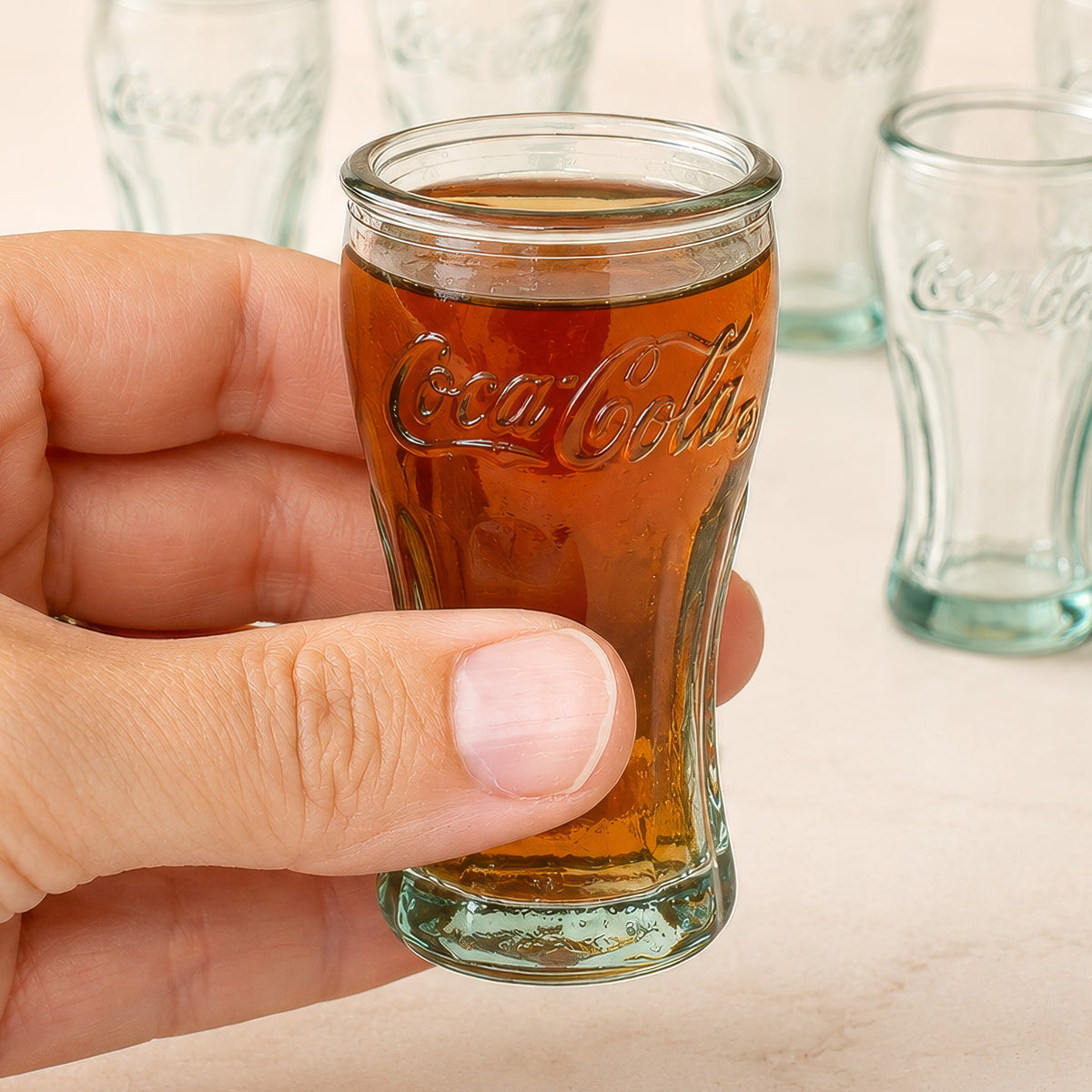 Coca-Cola Schnapsglas mit Getränk in der Hand, weitere leere Gläser im Hintergrund