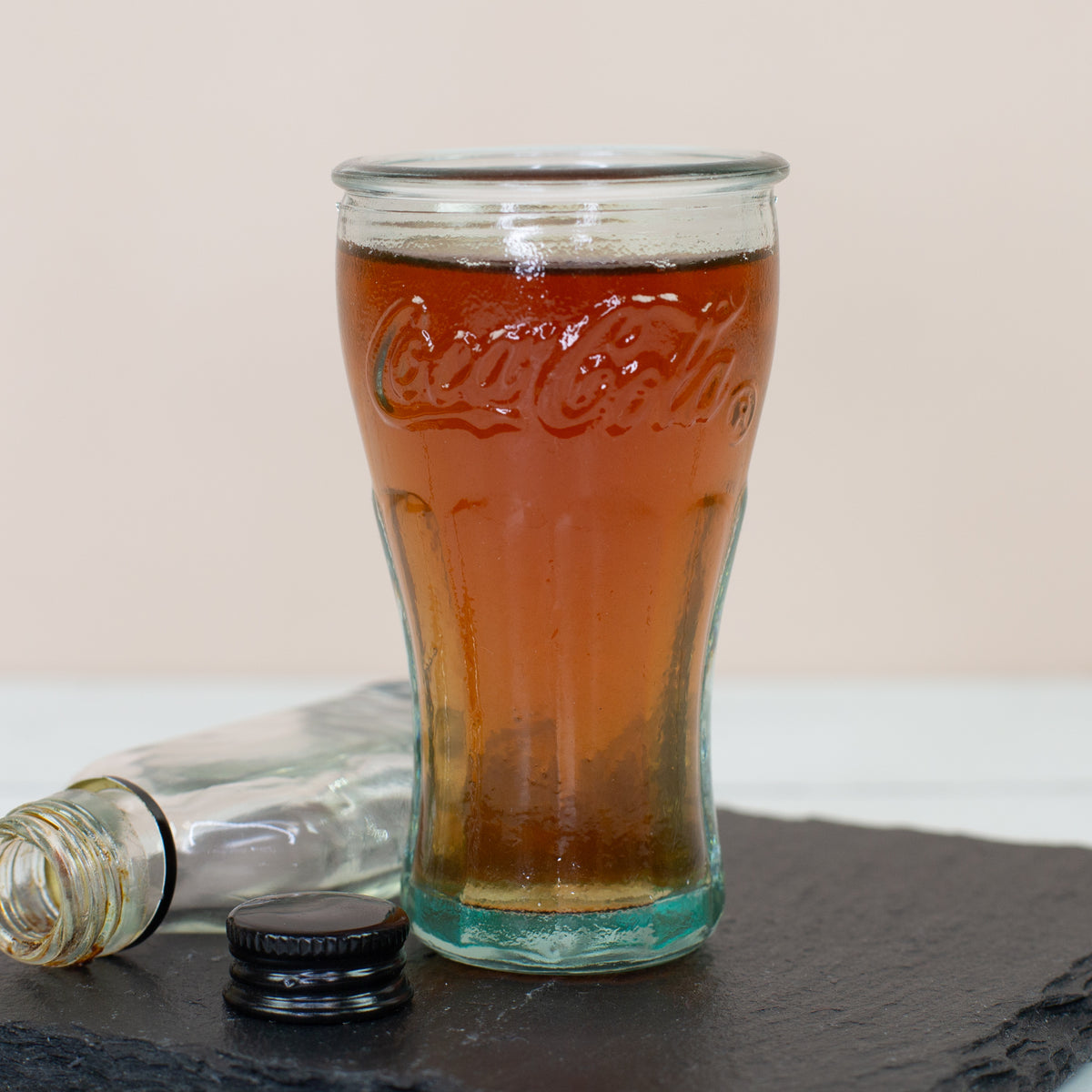 Gefülltes Coca-Cola Schnapsglas auf Schieferplatte mit kleiner Flasche im Hintergrund