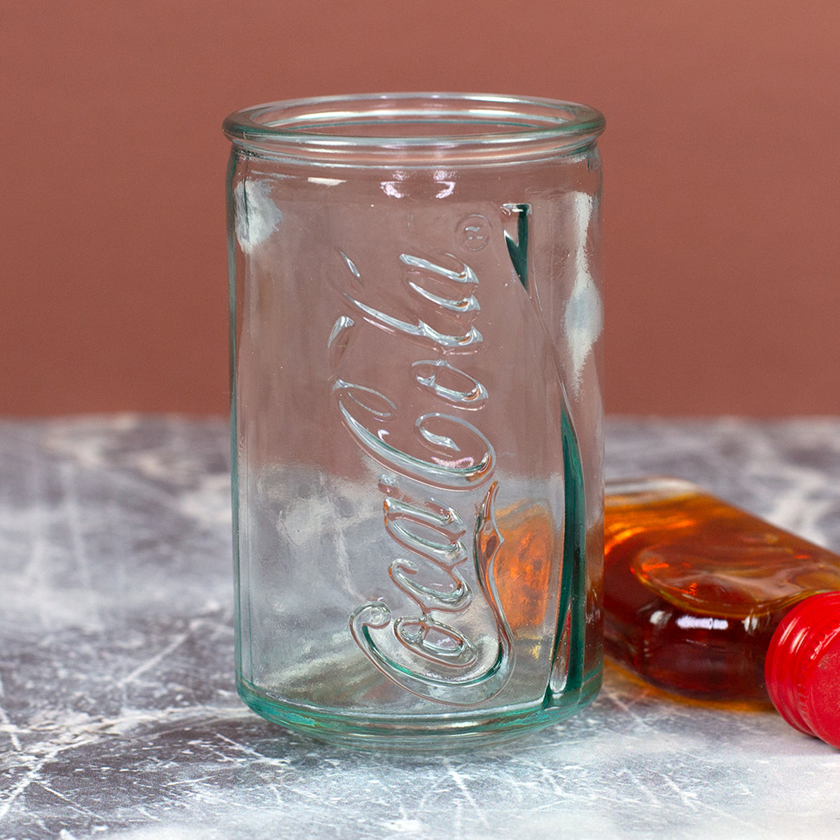 Aufrecht stehendes Coca-Cola Shotglas im Retro-Dosen-Look mit geprägtem Schriftzug und kleiner Flasche