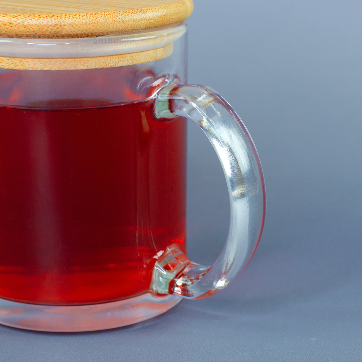 Nahaufnahme vom Glasgriff der Teeglastasse mit rotem Getränk und Bambusdeckel