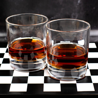 Zwei Whisky Gläser aus Borosilikatglas mit Whiskyfüllung auf Schachbrett