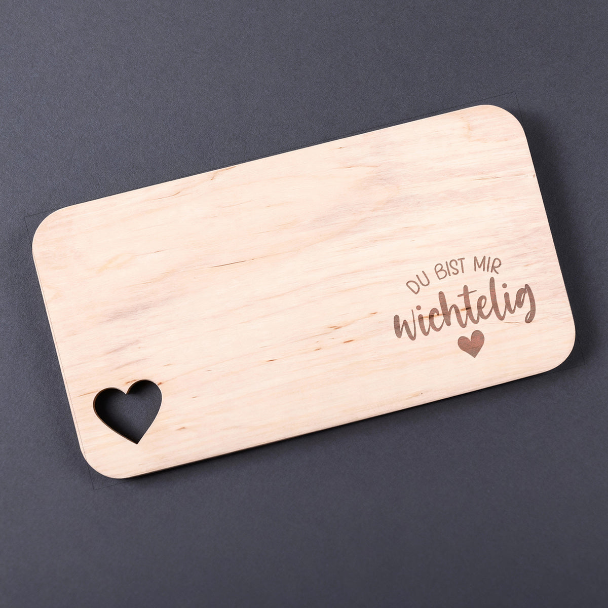 Holzbrettchen mit Spruch „Du bist mir wichtelig“ und Herzmotiv vor dunklem Hintergrund.