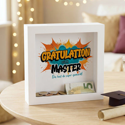 Geldgeschenk-Spardose „Gratulation zum Master“ im weißen Bilderrahmen auf festlicher Deko