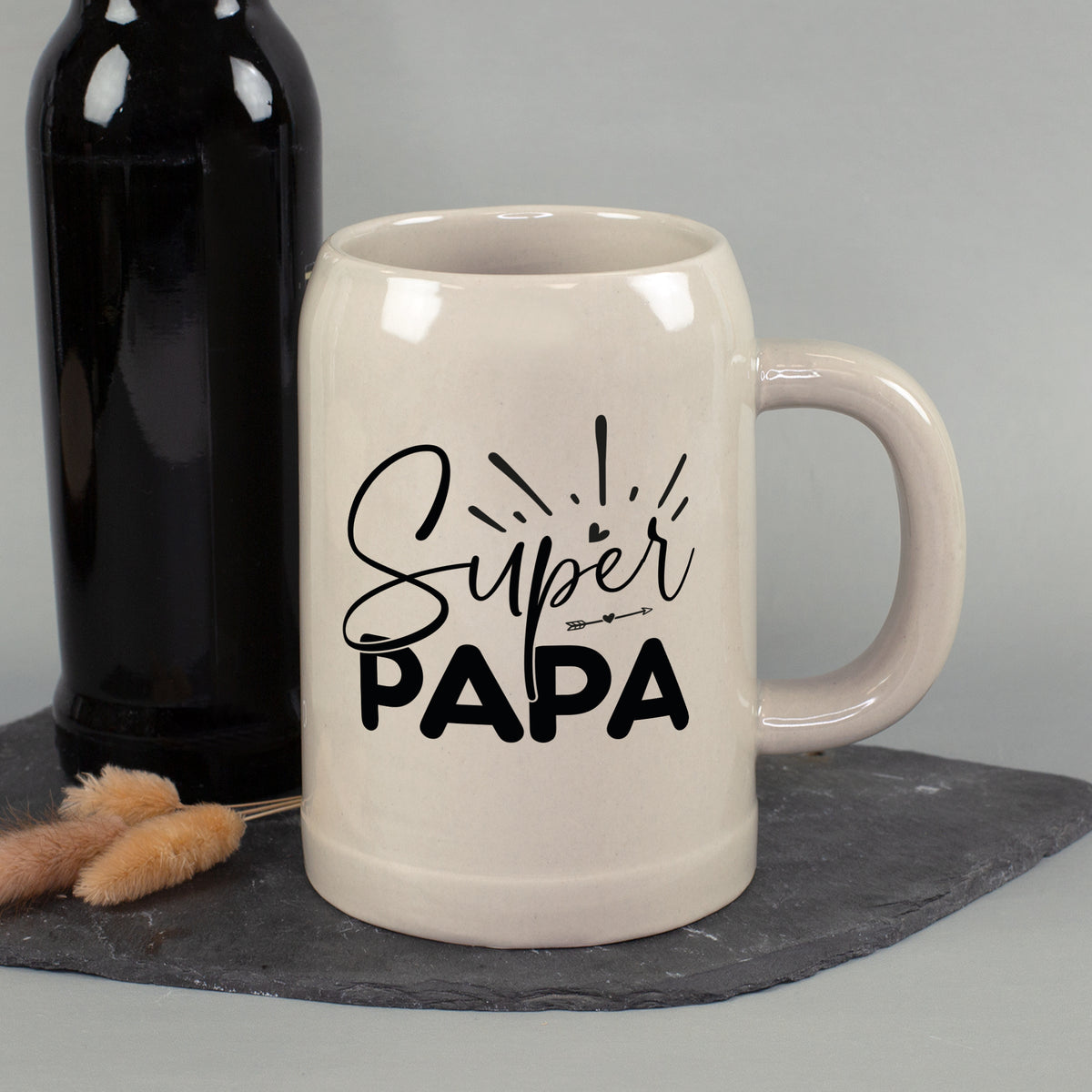 Bierkrug mit „Super Papa“-Aufdruck neben Bierflasche auf dunklem Untergrund