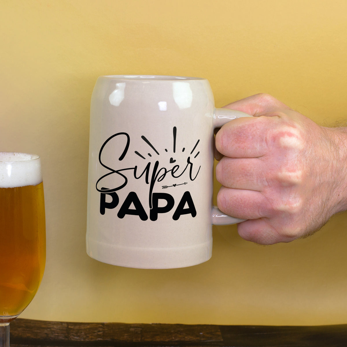 Bierkrug wird von Hand gehalten mit Bierglas im Hintergrund