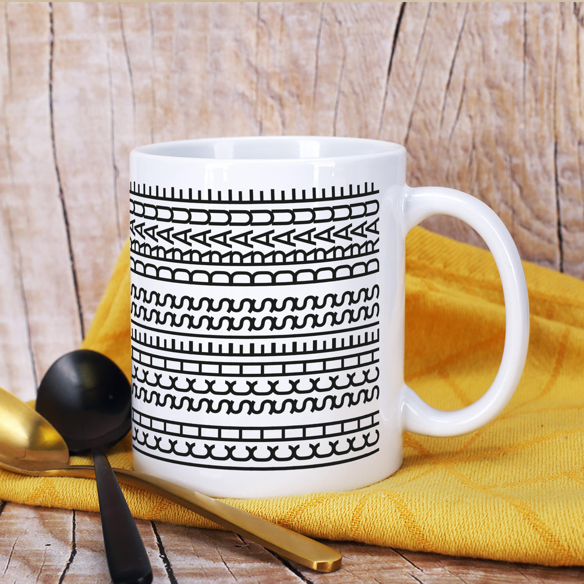 Lustige Keramiktasse mit verstecktem Schriftzug auf gelbem Tuch neben Besteck