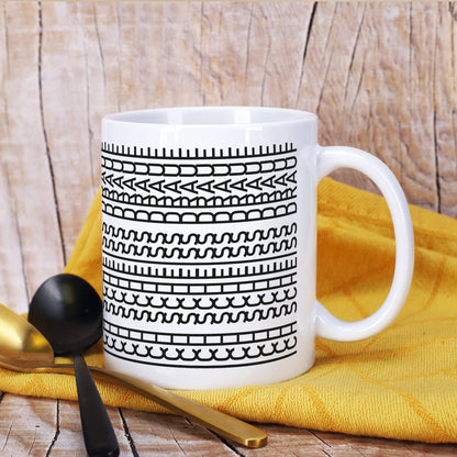 Lustige Keramiktasse mit verstecktem Schriftzug auf gelbem Tuch neben Besteck