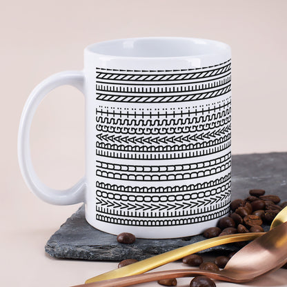 Weiße Tasse mit schwarzem Muster und versteckter Botschaft auf Schieferplatte mit goldenen Löffeln und Kaffeebohnen