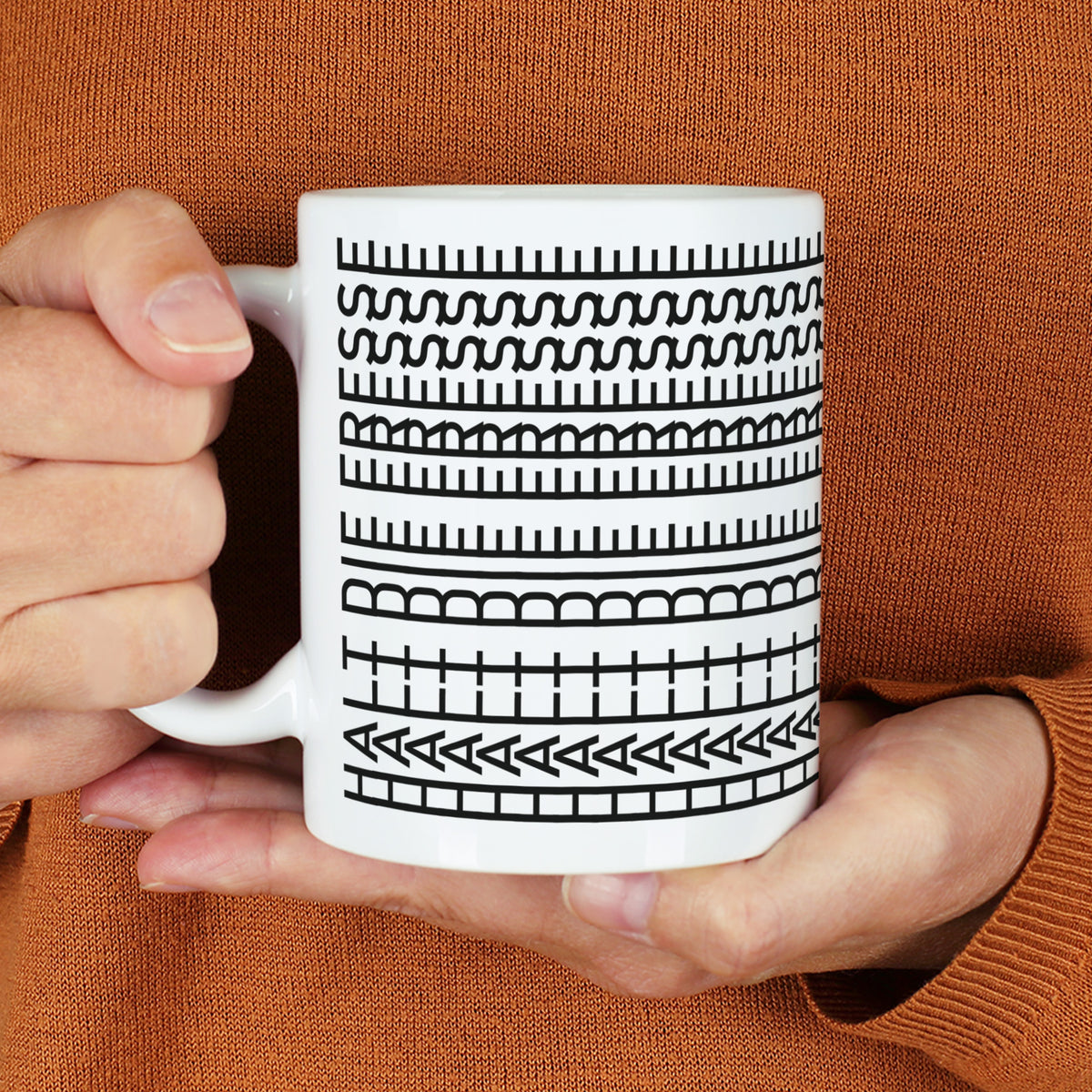 Weiße Tasse mit schwarzem Muster und verstecktem Spruch „Halt die Fresse“ in den Händen gehalten