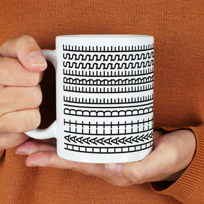Weiße Tasse mit schwarzem Muster und verstecktem Spruch „Halt die Fresse“ in den Händen gehalten