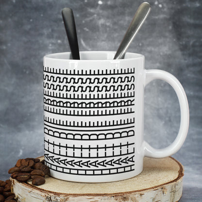 Keramiktasse mit grafischem Schwarz-Weiß-Muster, Löffeln und Kaffeebohnen auf Holzscheibe