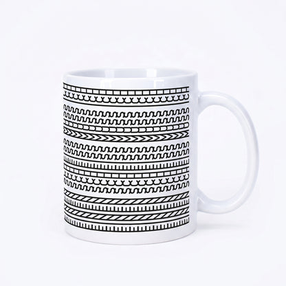 Weiße Kaffeetasse mit schwarzem grafischem Muster und versteckter Botschaft „Einen Scheiss muss ich“