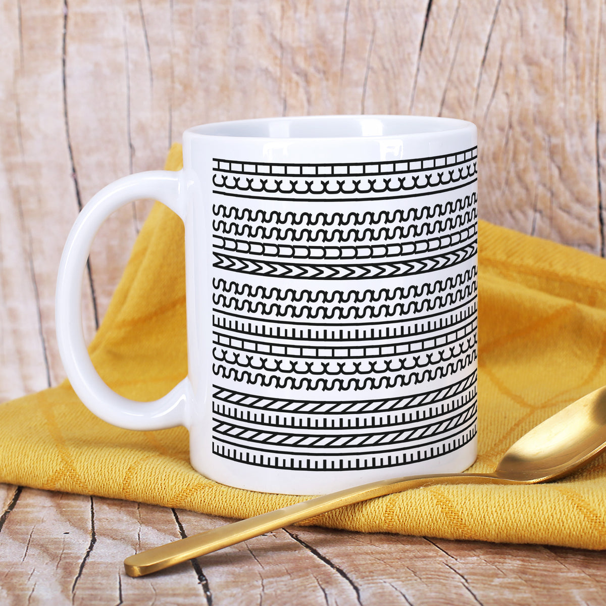 Weiße Keramiktasse mit Schwarz-Weiß-Muster auf Holzuntergrund und gelbem Tuch