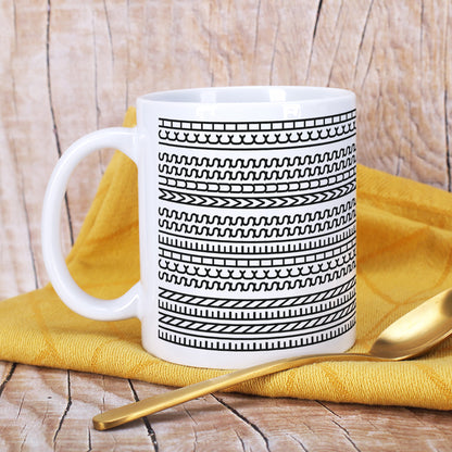 Weiße Keramiktasse mit Schwarz-Weiß-Muster auf Holzuntergrund und gelbem Tuch