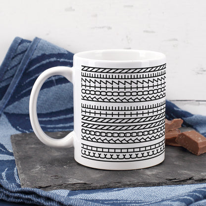 Kaffeetasse mit grafischem Schwarz-Weiß-Muster auf Schieferplatte neben blauem Tuch und Schokolade
