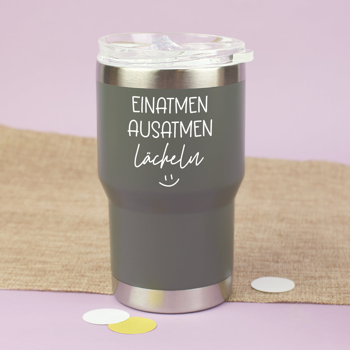 Grauer Thermobecher mit Deckel und Spruch Einatmen Ausatmen Lächeln auf hellem Hintergrund