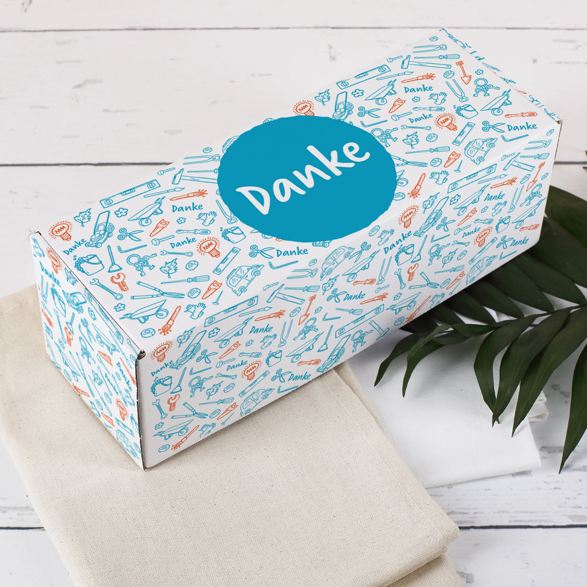 Dekorative Kartonbox mit Danke-Aufdruck auf heller Holzoberfläche mit Deko-Blatt