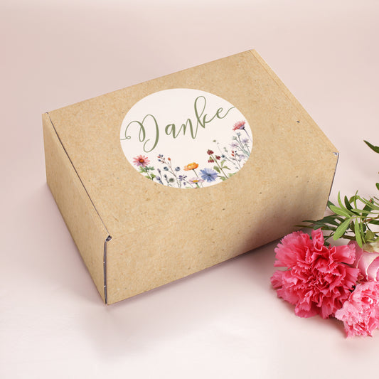 Mittelgroße Geschenkbox im floralen Kraftpapier-Look mit Aufschrift Danke, daneben pinke Nelken