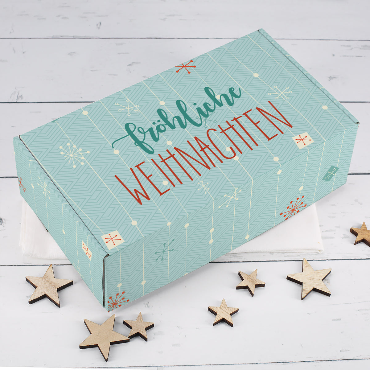 Türkise Geschenkbox zu Weihnachten mit grafischem Muster, roten Akzenten, Schneeflocken und Fröhliche Weihnachten Schriftzug