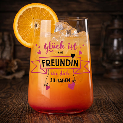 Trinkglas mit orangefarbenem Cocktail, Eiswürfeln, Orangenscheibe und Spruch „Glück ist eine Freundin wie dich zu haben“