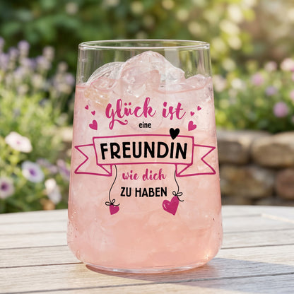 Trinkglas mit rosa Getränk, Eiswürfeln und Freundinnen-Motiv im sommerlichen Gartenambiente