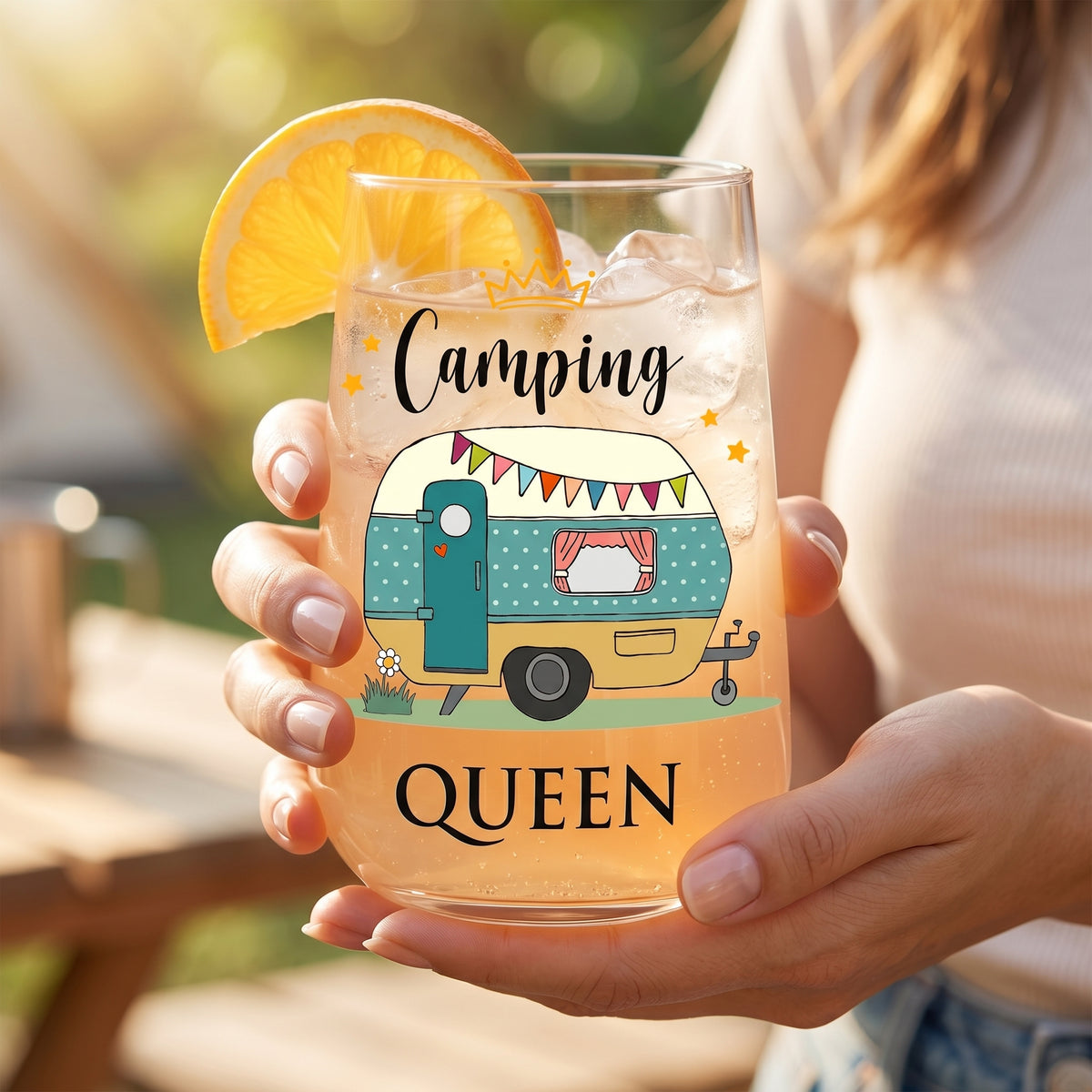 Trinkglas Camping Queen mit Wohnwagen-Motiv, Orangenscheibe und hellem Sommerdrink in der Hand