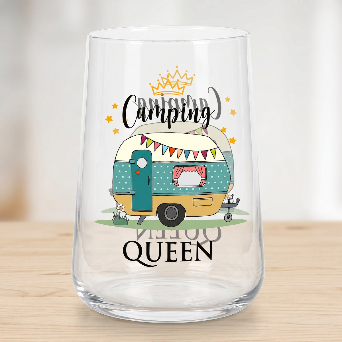 Leeres transparentes Trinkglas mit beidseitigem Camping Queen Motiv und Wohnwagen auf hellem Tisch