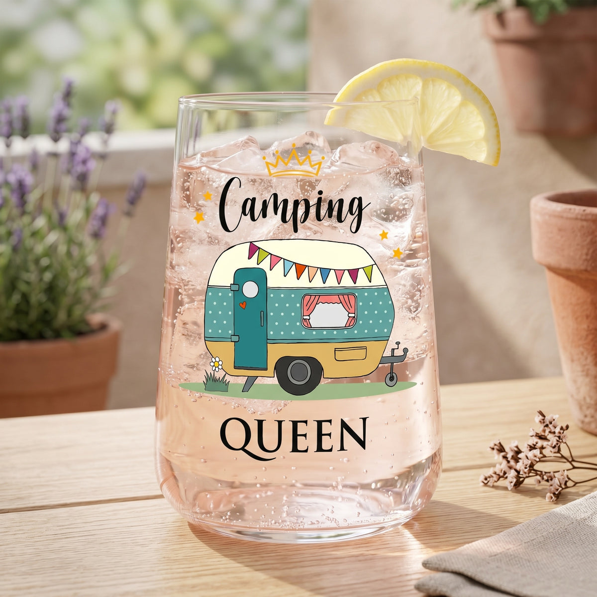 Trinkglas mit rosa Getränk, Eiswürfeln und Camping Queen Wohnwagen-Motiv auf Terrasse