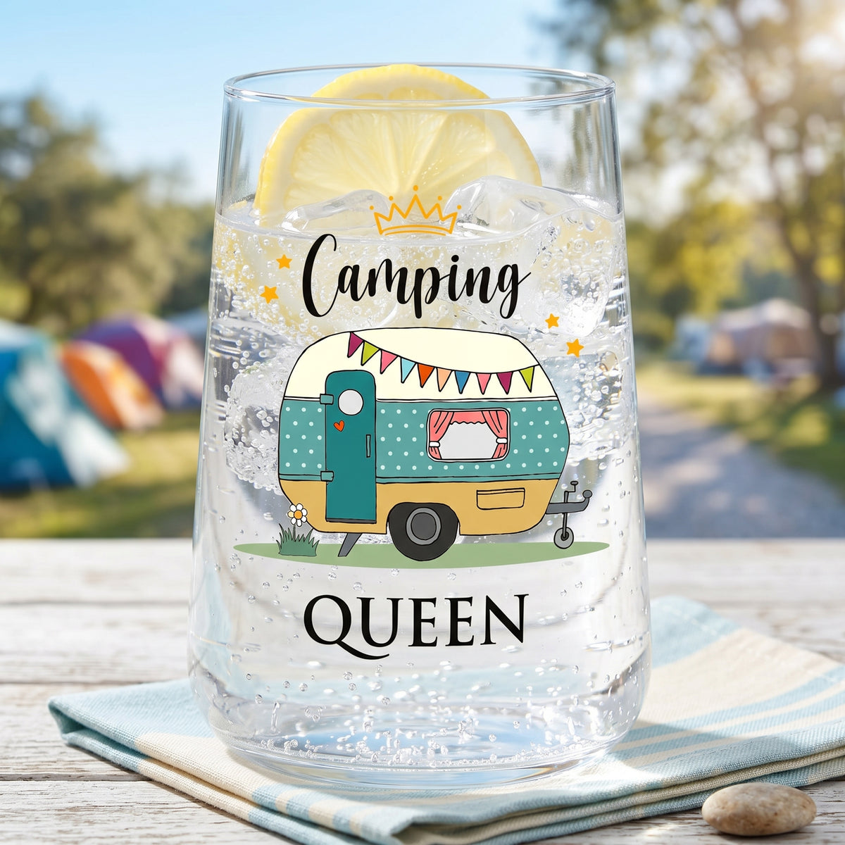 Trinkglas Camping Queen mit Wohnwagen, Zitronenscheibe und klarem Getränk auf Campingplatz