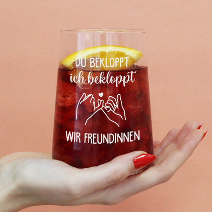Trinkglas mit rotem Getränk, Orangenscheibe und Spruch „Du bekloppt, ich bekloppt, wir Freundinnen“ in der Hand