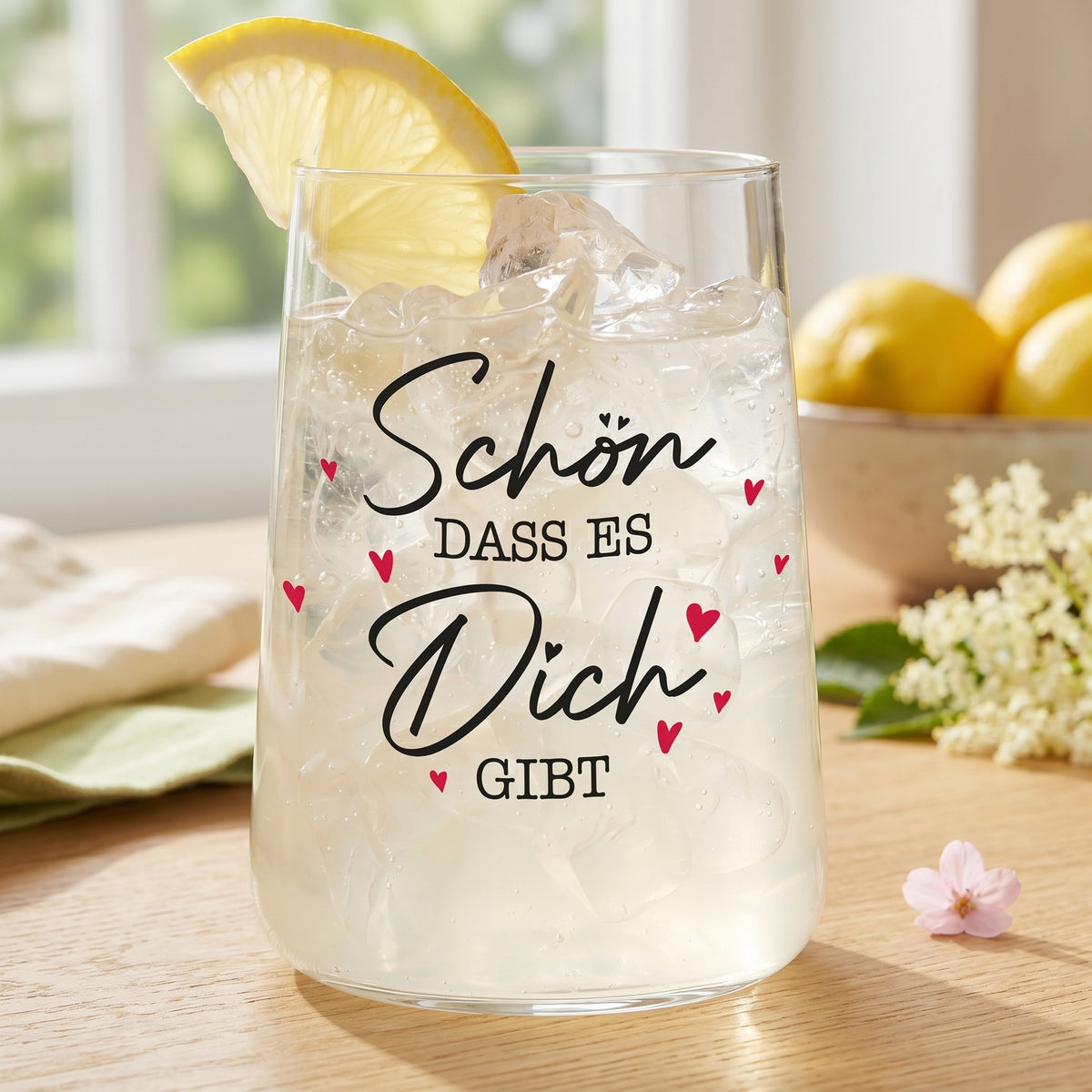 Trinkglas mit Zitronenscheibe, Eiswürfeln und Aufdruck Schön dass es Dich gibt auf Holztisch