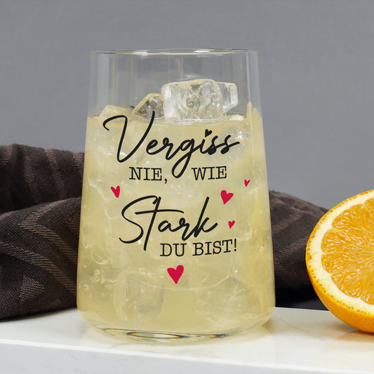 Trinkglas mit hellem Getränk, Eiswürfeln und Aufdruck Vergiss nie wie stark du bist neben Orangenscheibe
