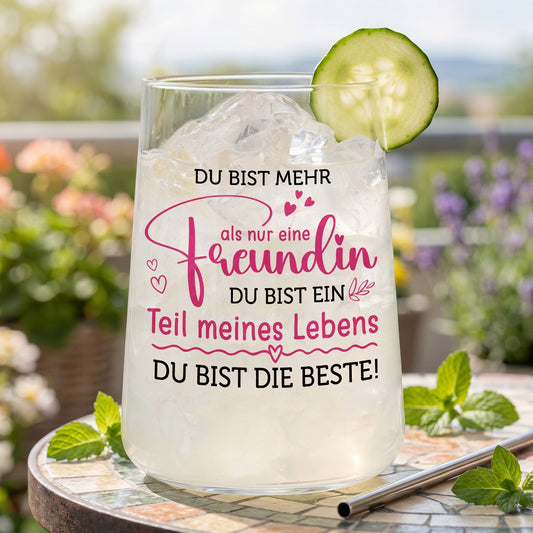 Limoglas mit Freundinnen-Spruch in Pink und Schwarz, gefüllt mit Eis und Gurkenscheibe auf sommerlichem Gartentisch
