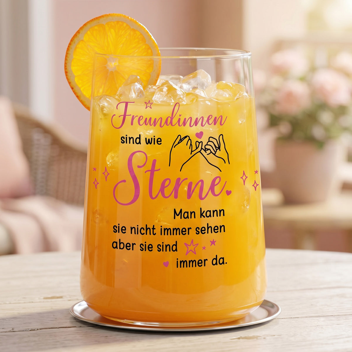 Trinkglas mit Motiv „Freundinnen sind wie Sterne“ gefüllt mit orangem Getränk und Orangenscheibe auf hellem Tisch im wohnlichen Ambiente