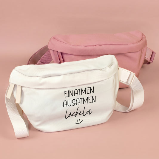 Bauchtasche mit Spruch Einatmen Ausatmen Lächeln in Creme vor rosa Bauchtasche auf rosafarbenem Hintergrund