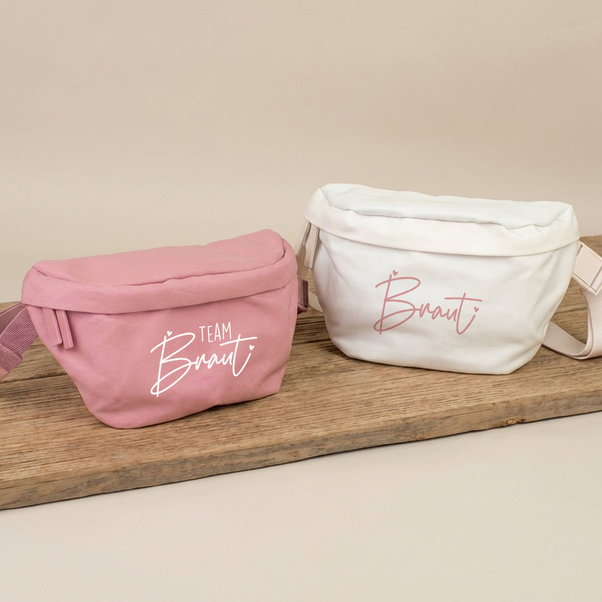 Rosa JGA Bauchtasche mit Aufdruck Team Braut und cremefarbene Bauchtasche mit Aufdruck Braut auf Holzbrett