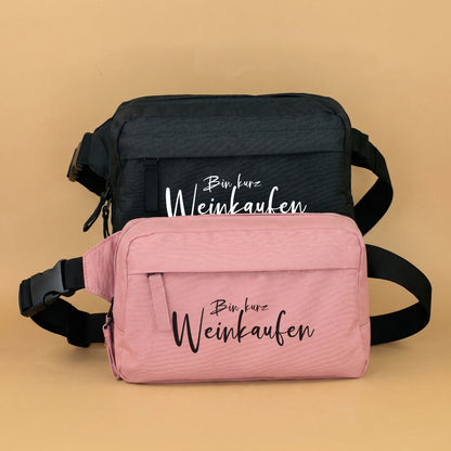 Bauchtasche mit Spruch Bin kurz Weinkaufen in Rosa und Schwarz vor beigem Hintergrund