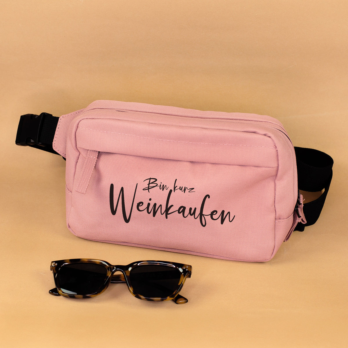 Rosa Bauchtasche mit Spruch Bin kurz Weinkaufen und schwarzem Gurt auf weißem Hintergrund
