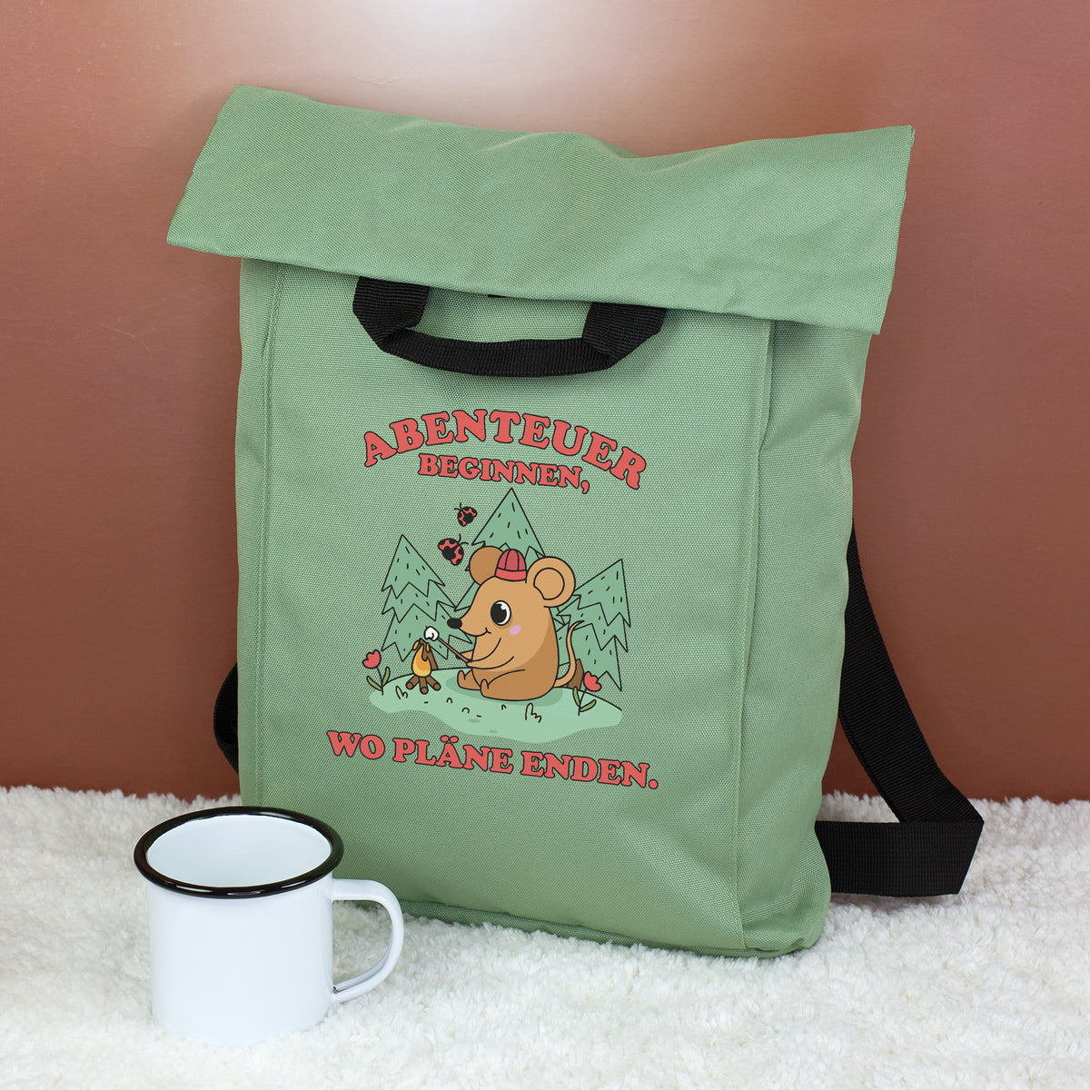 Jadegrüner Rucksack mit Abenteuer-Maus Motiv, Campingmaus, Bergen und Spruch auf flauschigem Untergrund