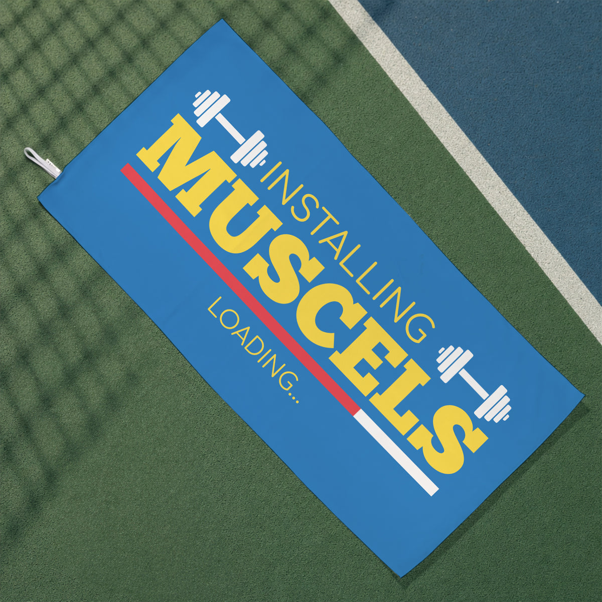 Blaues Gym Handtuch mit Hantelmotiv und Installing Muscles Loading Schriftzug auf Sportplatz